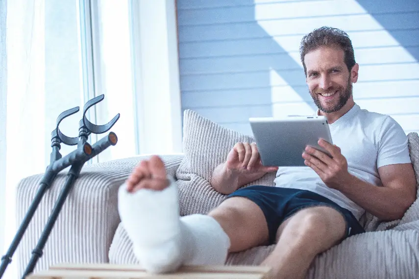 Un homme souriant, assis sur son canapé avec un pied dans le plâtre, confiant grâce à une couverture prévoyance.