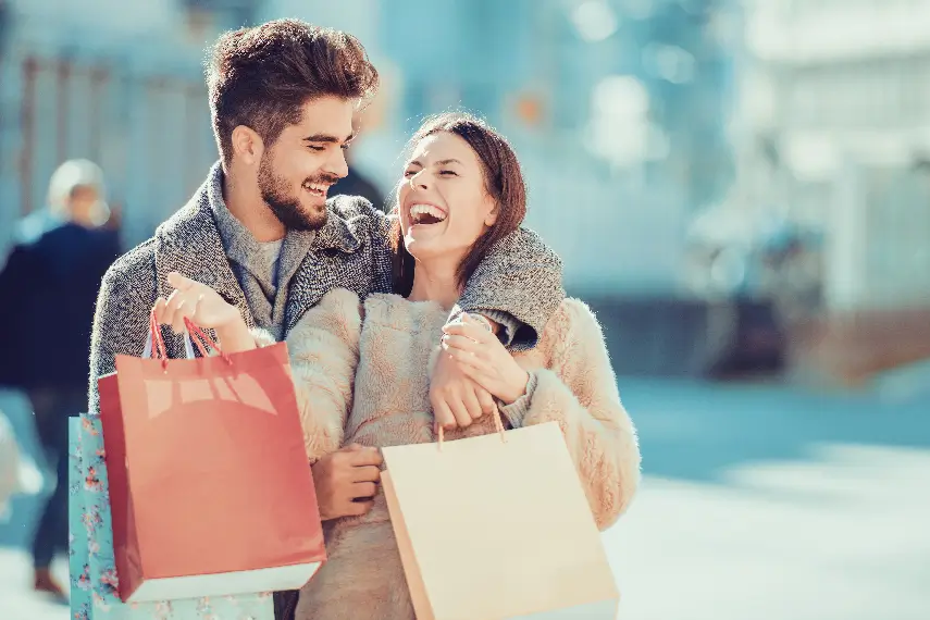 Un couple souriant, les bras chargés de sacs, profitant d’une session de shopping ensemble.