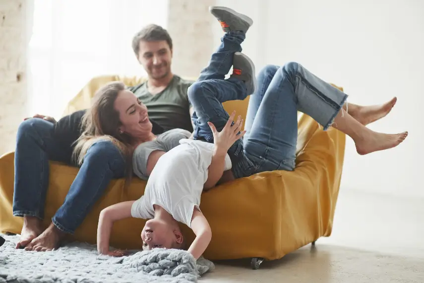 Une famille souriante sur un canapé, où la jeune fille fait le poirier dans une ambiance pleine de joie et de sérénité.