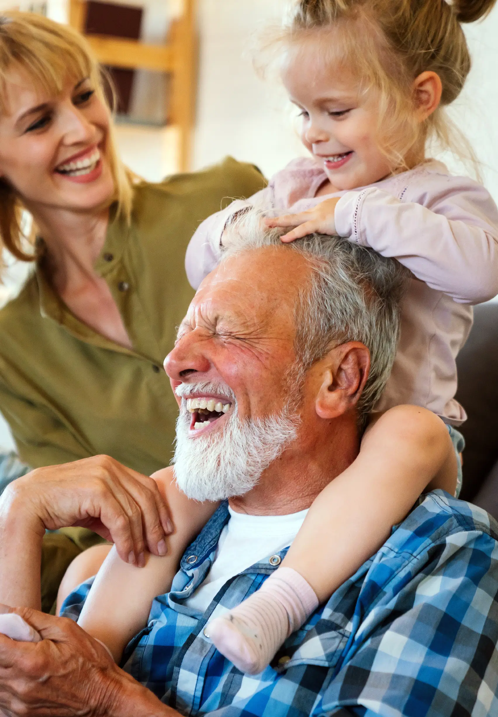 Grand-père heureux portant sa petite-fille sur les épaules aux côtés de sa fille.
