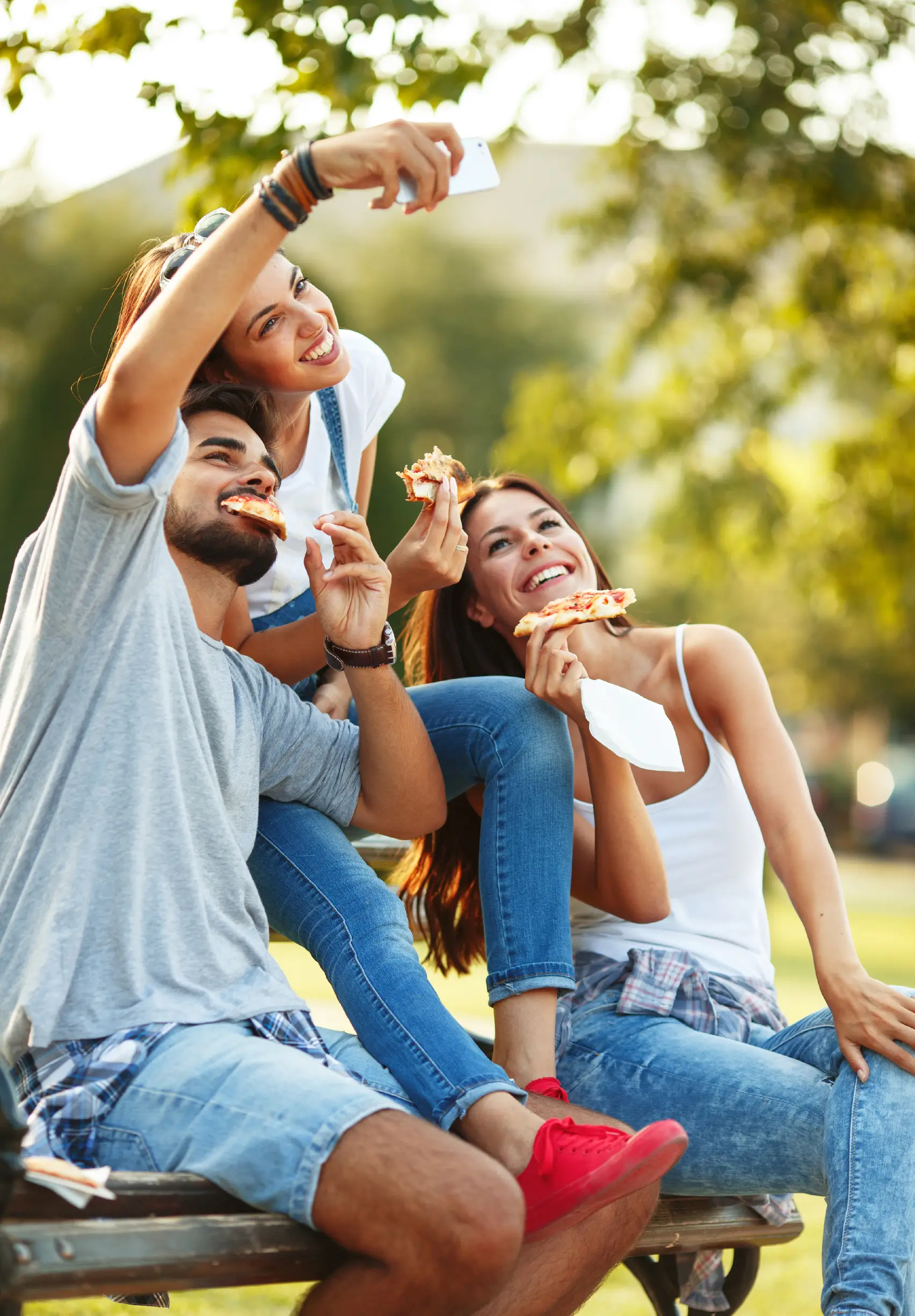 Groupe de jeunes sur un banc, partageant un repas rapide et capturant l’instant en selfie.