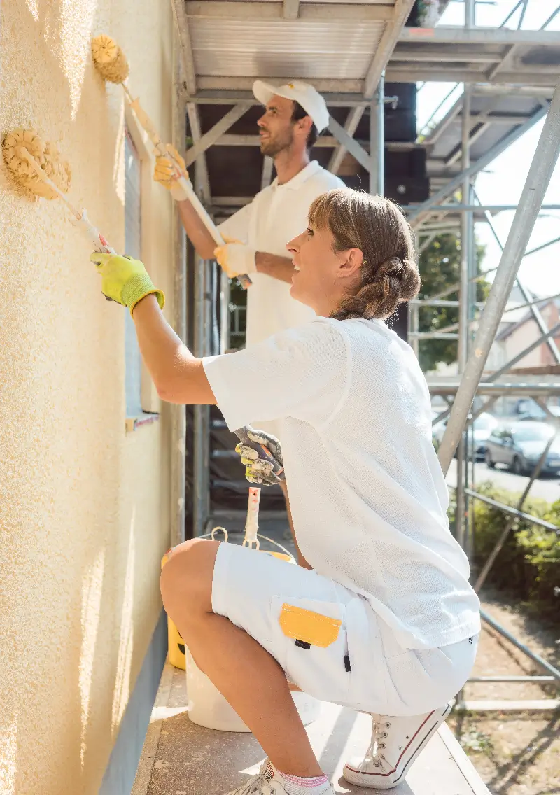 Deux artisans peintres en train de rénover une façade de bâtiment.