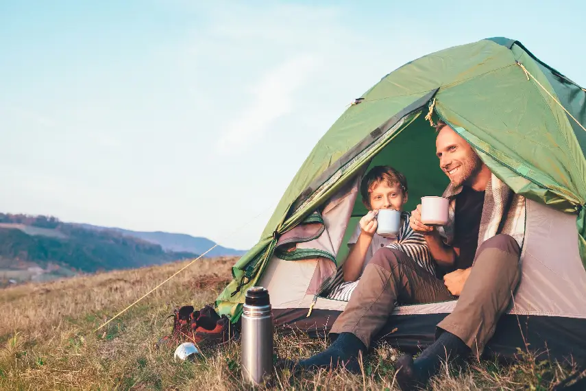 Papa et fils prennent leur petit déjeuner en pleine nature après une nuit de camping, avec une mutuelle prévoyance pour toute la famille.
